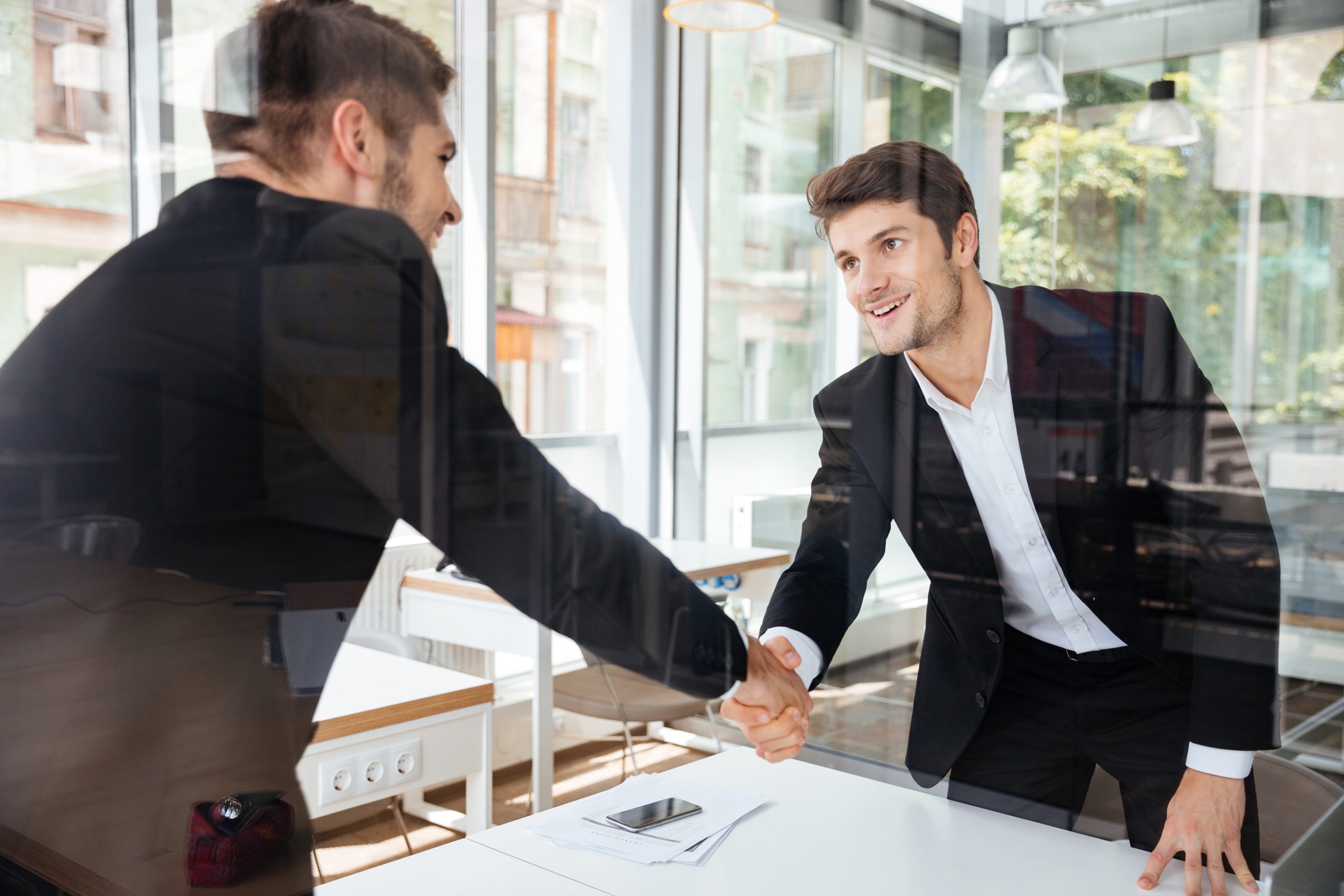 graphicstock two happy successful young businessmen standing and shaking hands on business meeting rdzlG mH3x scaled